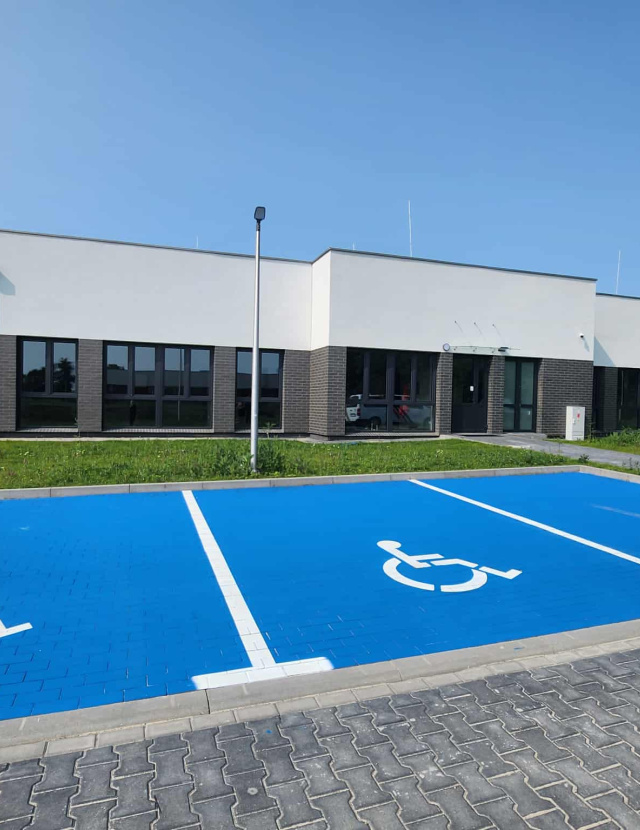Przed pięknym, nowoczesnym domem znajdują się miejsca parkingowe dla osób niepełnosprawnych.