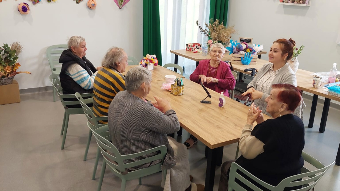 Grupa seniorów siedzi przy stole i wspólnie wykonuje prace ręczne