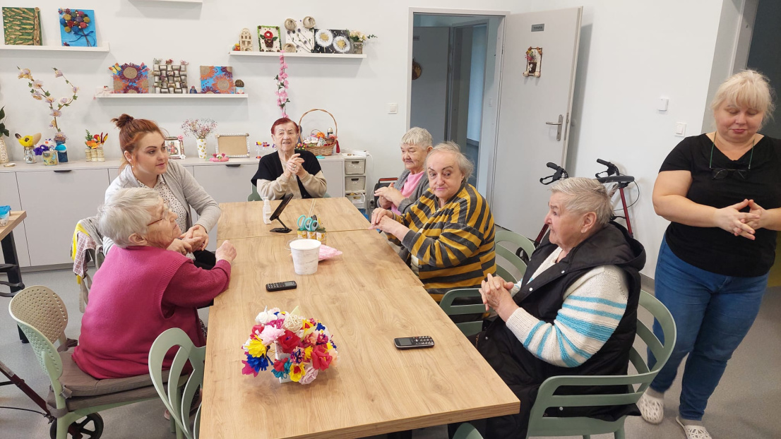 Nowoczesna, jasna sala z dużą przestrzenią, kilka osób siedzi przy stole i rozmawia