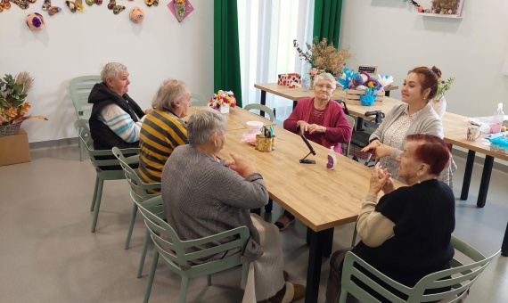Grupa seniorów siedzi przy stole i wspólnie wykonuje prace ręczne