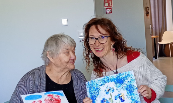 Młoda kobieta i starsza kobieta siedzą przy stole, prezentując swoje wspaniałe dzieła sztuki.